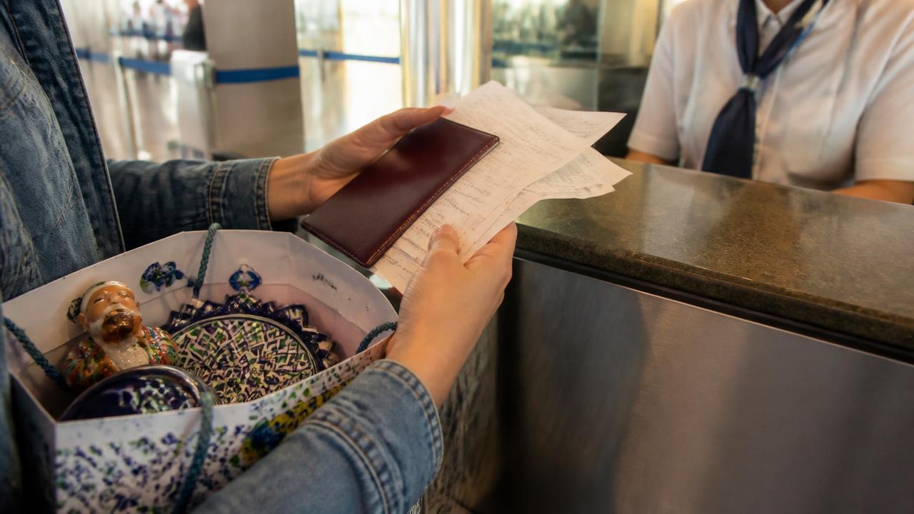 A traveller holding a passport and a handful of shop receipts at an airport tax refund desk, with a paper bag of Uzbek ceramic souvenirs in the foreground.